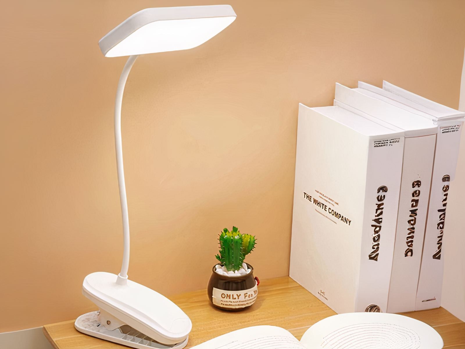 Liseuse LED à pince et rechargeable, posée sur un bureau à côté de livres.