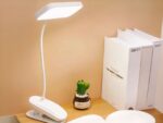 Liseuse LED à pince et rechargeable, posée sur un bureau à côté de livres.
