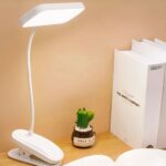 Liseuse LED à pince et rechargeable, posée sur un bureau à côté de livres.