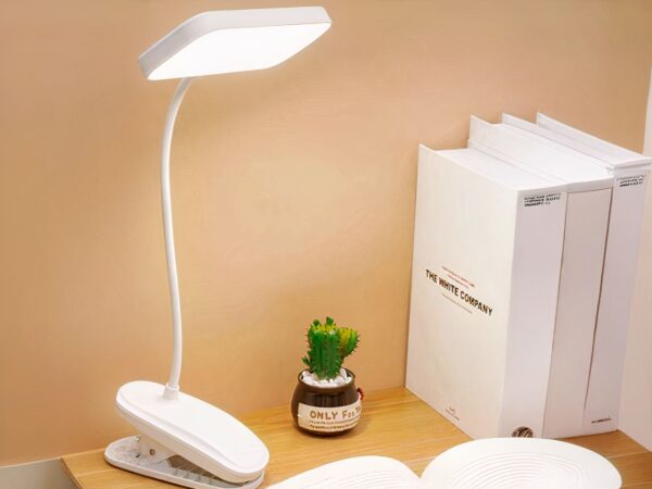 Liseuse LED à pince et rechargeable, posée sur un bureau à côté de livres.