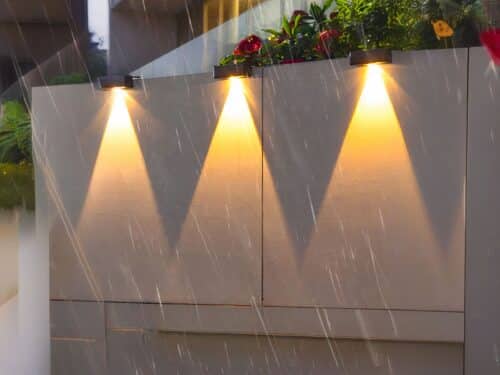Applique LED solaire étanche et design noir, au nombre de 3 avec lumière jaune sur un mur.