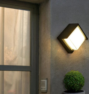 Applique murale exterieur LED imperméable et moderne installée sur un mur avec une plante verte en dessous et une porte vitrée à gauche