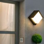 Applique murale extérieur LED imperméable et moderne Applique murale exterieur LED imperméable et moderne installé sur un mur avec une porte vitrée à gauche et une plante verte en dessous