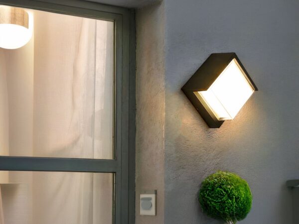 Applique murale exterieur LED imperméable et moderne installé sur un mur avec une porte vitrée à gauche et une plante verte en dessous