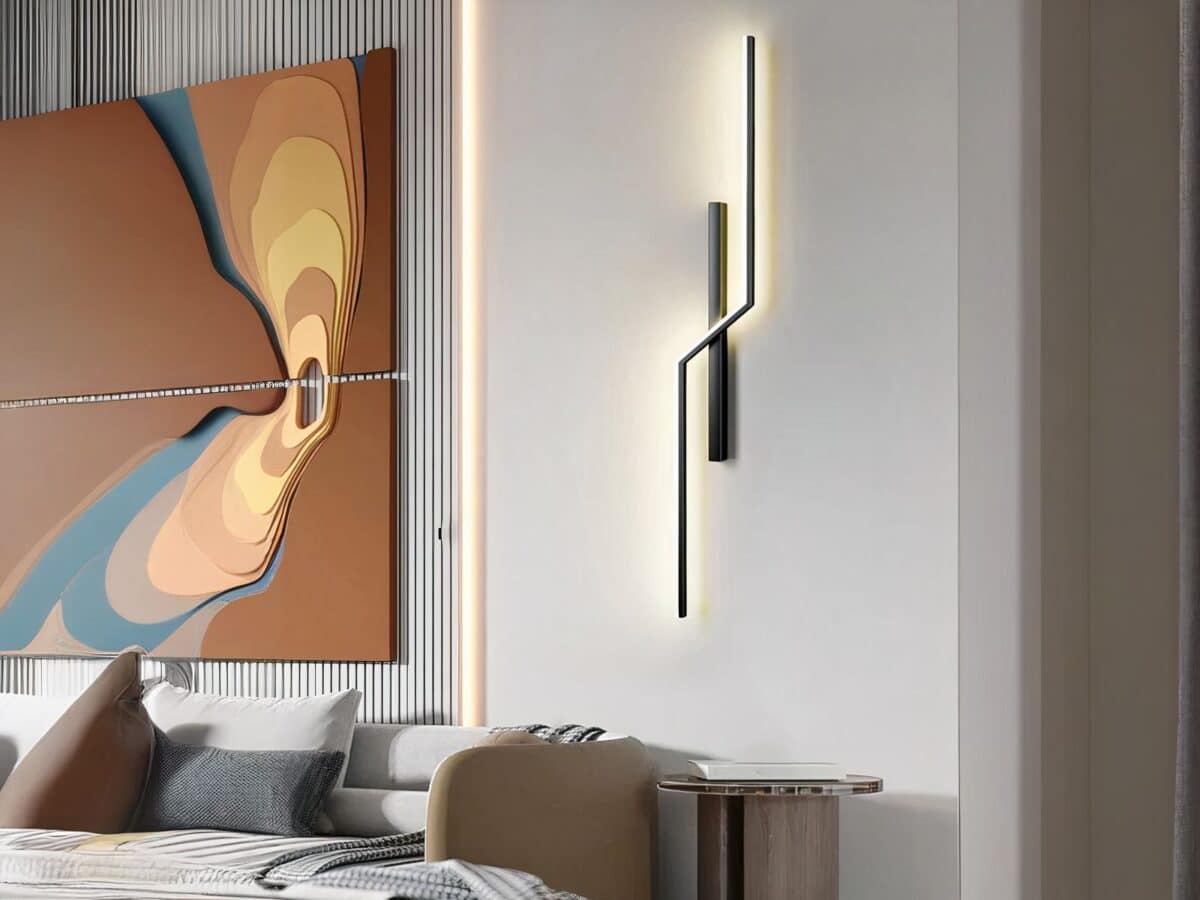 Applique murale LED minimaliste linéaire moderne Applique murale LED minimaliste moderne noir, allumée et installée verticalement sur un mur gris clair à côté d'une grande œuvre d'art en forme de tableau.