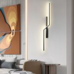 Applique murale LED minimaliste linéaire moderne Applique murale LED minimaliste moderne noir, allumée et installée verticalement sur un mur gris clair à côté d'une grande œuvre d'art en forme de tableau.