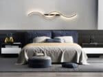 Chambre avec grand lit, une belle tête de lit bleu foncé en velours. Au-dessus, une applique murale LED noire moderne double S à l'horizontale.