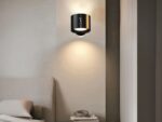 Applique murale LED noire, fixé au mur à côté d'un lit, en guise de lampe de chevet. La lumière est projetée par en haut et an bas.
