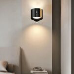 Applique murale LED sans fil rotative Applique murale LED noire, fixé au mur à côté d'un lit, en guise de lampe de chevet. La lumière est projetée par en haut et an bas.