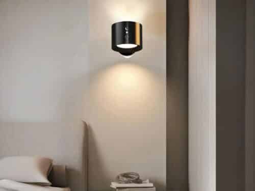 Applique murale LED noire, fixé au mur à côté d'un lit, en guise de lampe de chevet. La lumière est projetée par en haut et an bas.