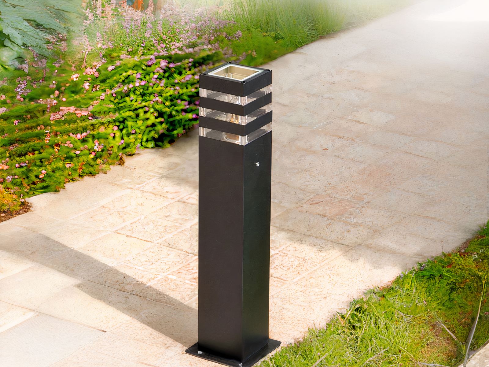 Borne extérieure LED design noir et étanche, sur une allée à côté de l'herbe.