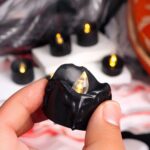 Bougie LED noire, mini, dans les doigts d'une personne.