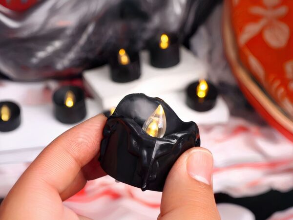 Bougie LED noire, mini, dans les doigts d'une personne.