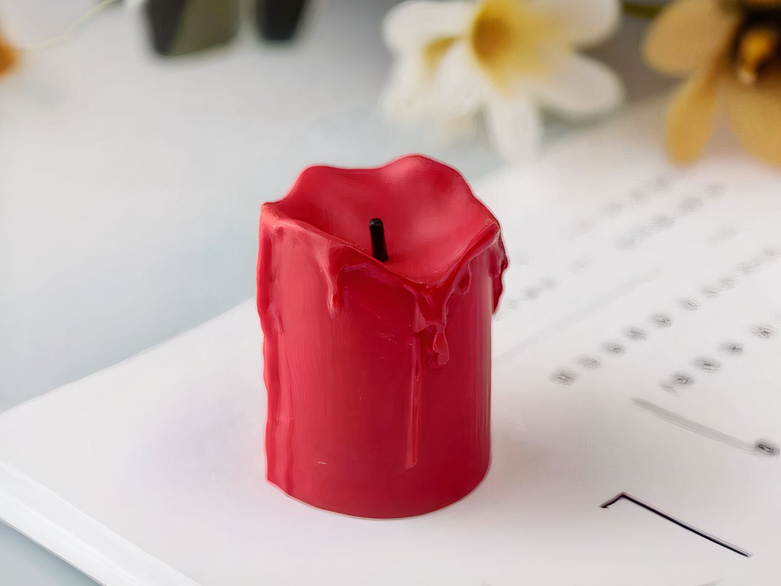 Petite bougie LED rouge effet fondu posée sur un magazine.