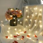 Guirlande LED à pile avec étoiles Guirlande LED à pile, posée en décoration sur un tulle blanc et un bouquet de fleur dans un vase.