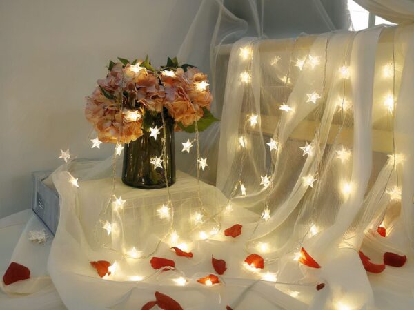 Guirlande LED à pile, posée en décoration sur un tulle blanc et un bouquet de fleur dans un vase.