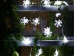 Guirlande LED à piles avec des flocons de neige illuminés, installées sur une structure en métal avec des feuilles de sapin synthétiques dans l'obscurité.