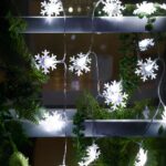 Guirlande LED à pile avec flocons de neige Guirlande LED à piles avec des flocons de neige illuminés, installées sur une structure en métal avec des feuilles de sapin synthétiques dans l'obscurité.