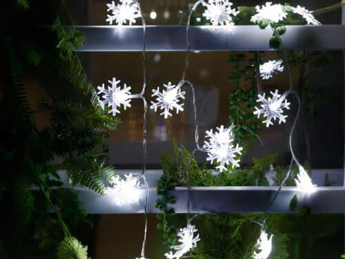 Guirlande LED à piles avec des flocons de neige illuminés, installées sur une structure en métal avec des feuilles de sapin synthétiques dans l'obscurité.