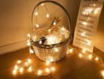 Guirlande LED à piles avec petites boules illuminées posée sur un panier en osier.