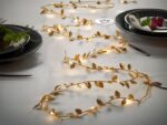 Guirlande LED à piles, doré ornée de feuilles, allumée et disposée comme chemin de table.
