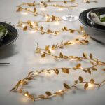 Guirlande LED à piles, doré ornée de feuilles, allumée et disposée comme chemin de table.