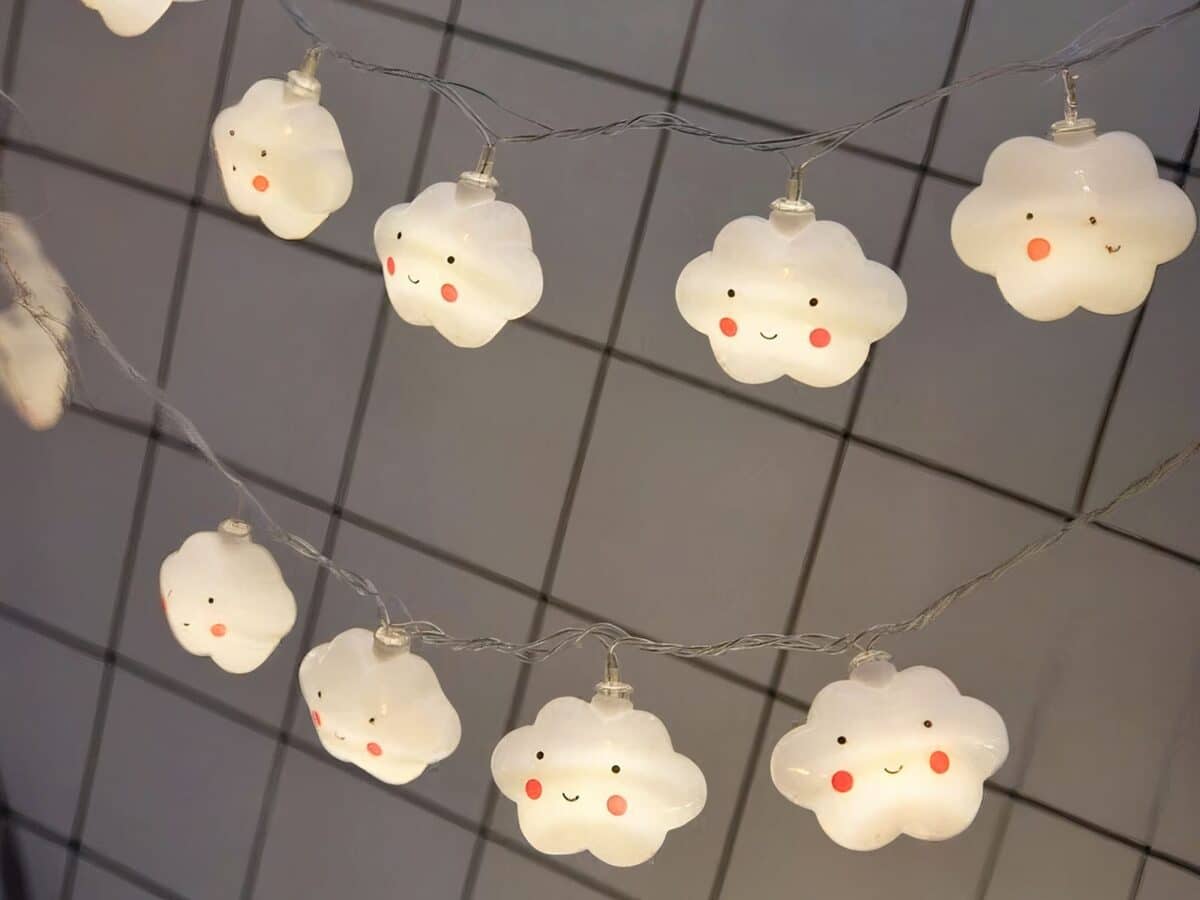 Guirlande LED à pile nuages sourires Guirlande LED à piles, avec des nuages qui ont un visage dessiné, installé sur un quadrillage métallique.
