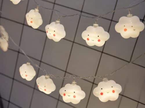 Guirlande LED à piles, avec des nuages qui ont un visage dessiné, installé sur un quadrillage métallique.