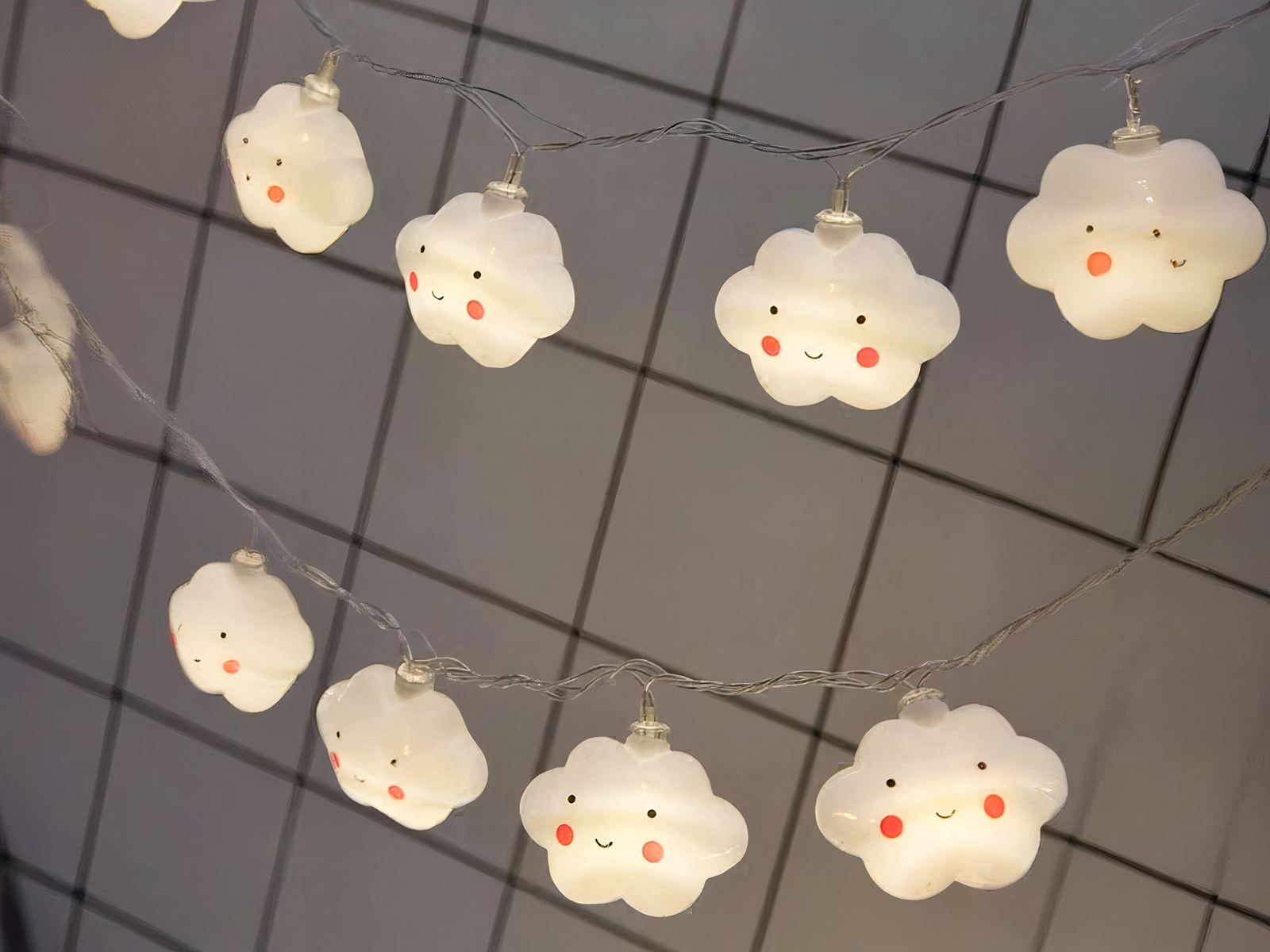 Guirlande LED à pile nuages avec sourires Guirlande LED à piles, avec des nuages qui ont un visage dessiné, installé sur un quadrillage métallique.