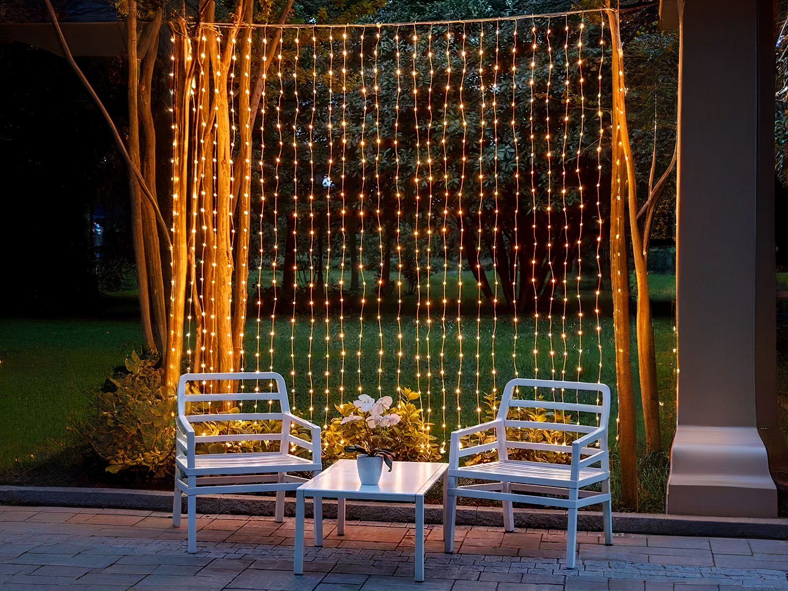 Guirlande LED solaire style rideau lumineux installée entre deux arbres avec une table et des chaises devant et une foret en fond