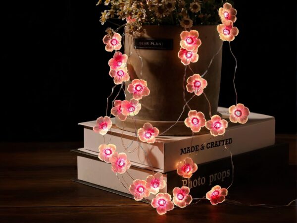 Guirlande mini LED design en forme de fleurs roses, sur des livres et un pot de fleur.