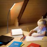 Enfant assit à un bureau et dessine, à côté est installé le lampadaire LED col de cygne réglable.