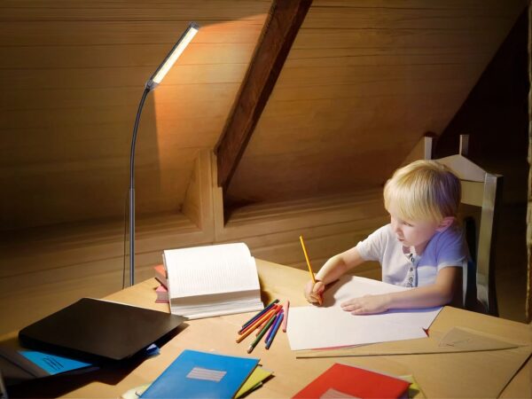 Enfant assit à un bureau et dessine, à côté est installé le lampadaire LED col de cygne réglable.