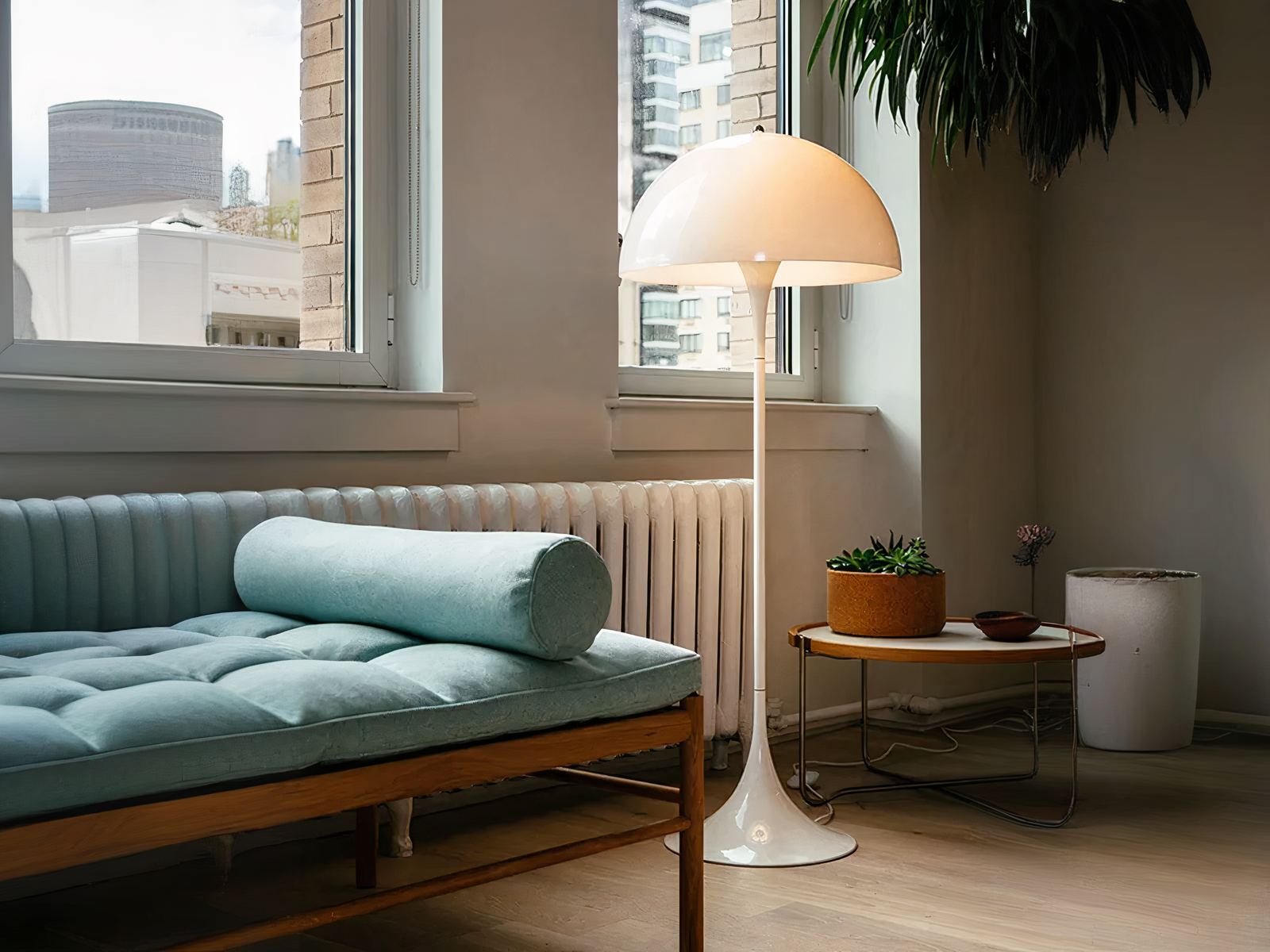 Lampadaire LED champignon blanc, installé dans un salon, à côté d'un chauffage et d'un sofa avec des coussins vert.