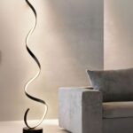 Lampadaire LED design moderne en spirale Lampadaire LED noir, design moderne en spirale, allumé et posé à côté d'un canapé gris foncé.