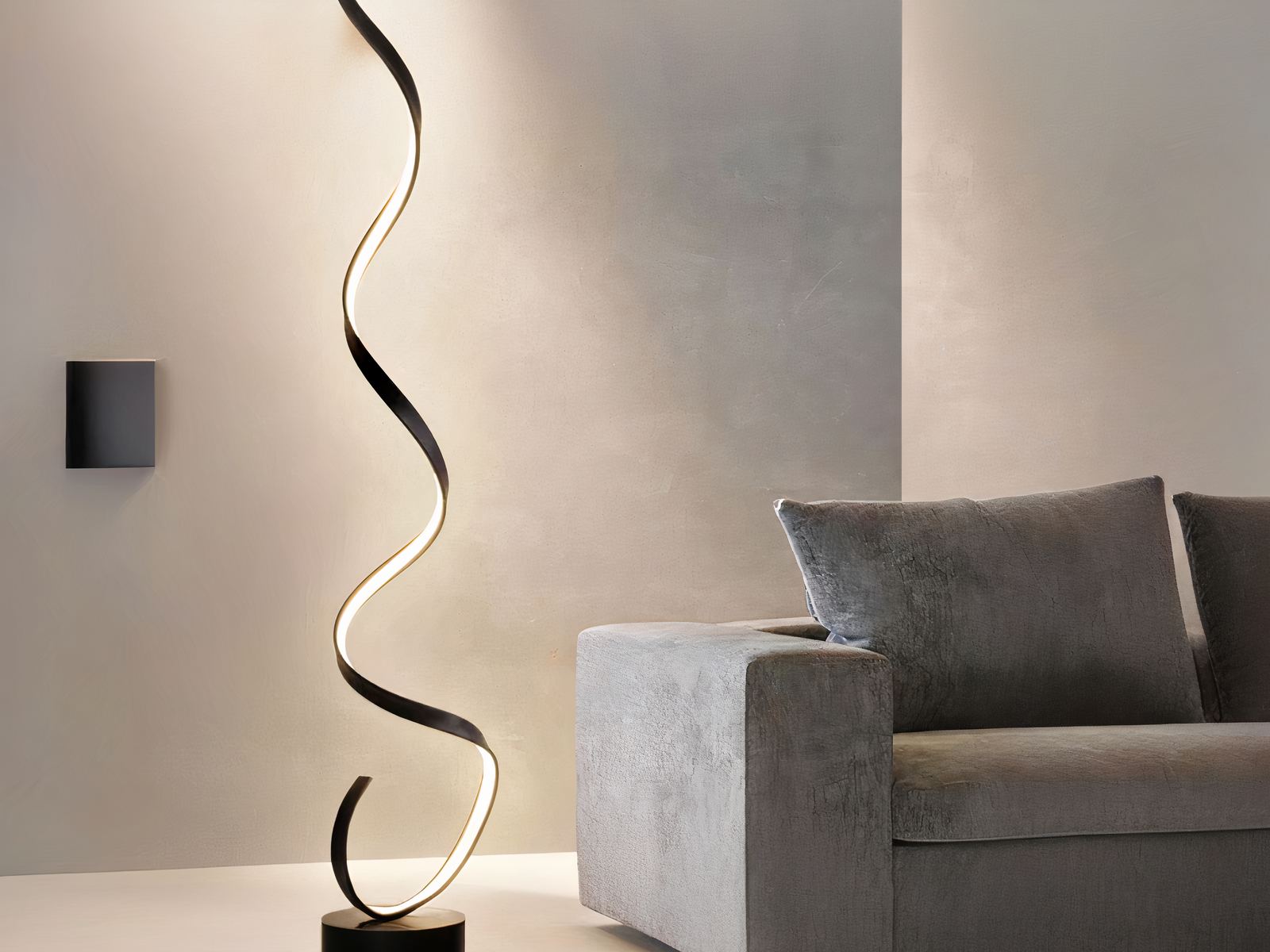Lampadaire LED design moderne en spirale Lampadaire LED noir, design moderne en spirale, allumé et posé à côté d'un canapé gris foncé.
