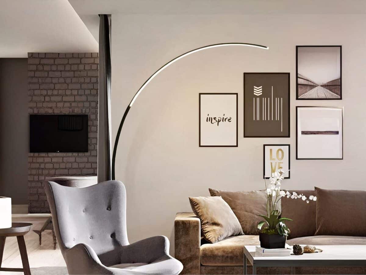 Lampadaire LED en arc-de-cercle minimaliste et moderne Lampadaire LED en arc-de-cercle noir, allumé et installé dans un salon à côté d'un canapé et d'un fauteuil.