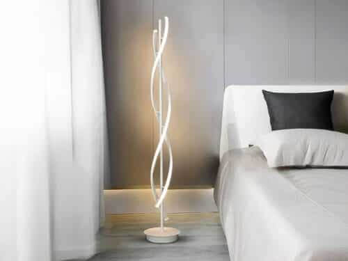 Lampadaire LED blanc, en spirale au design moderne, installé à côté d'un lit.