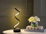 Lampe à poser LED noire à spirale, sur une table blanche.