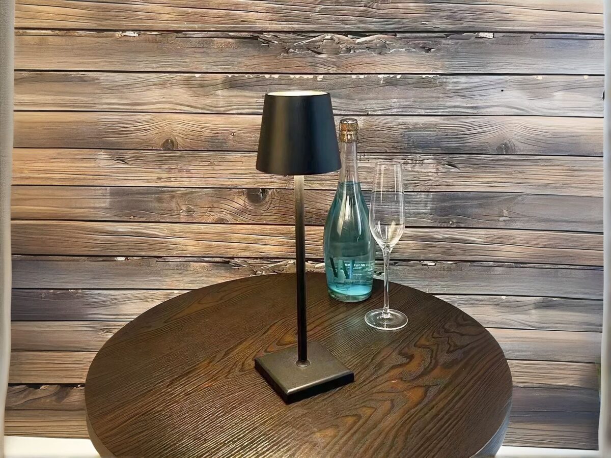 Lampe à poser LED noire tactile et rechargeable, sur une table ronde marron.