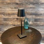 Lampe à poser LED noire tactile et rechargeable Lampe à poser LED noire tactile et rechargeable, sur une table ronde marron.