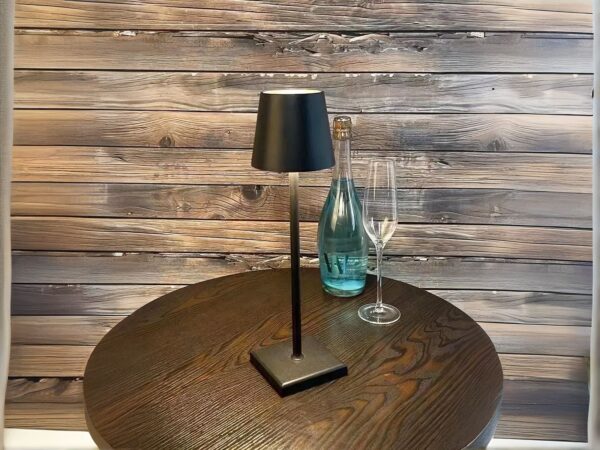 Lampe à poser LED noire tactile et rechargeable, sur une table ronde marron.