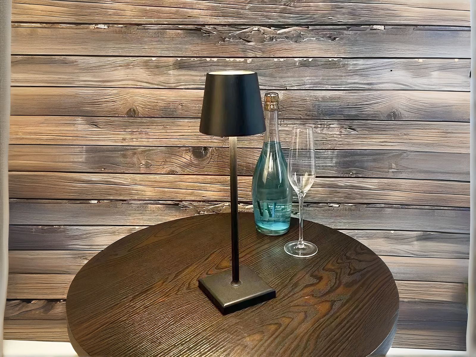 Lampe à poser LED noire tactile et rechargeable, sur une table ronde marron.