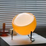 Lampe à poser LED orange tactile et sphérique, sur une table blanche.