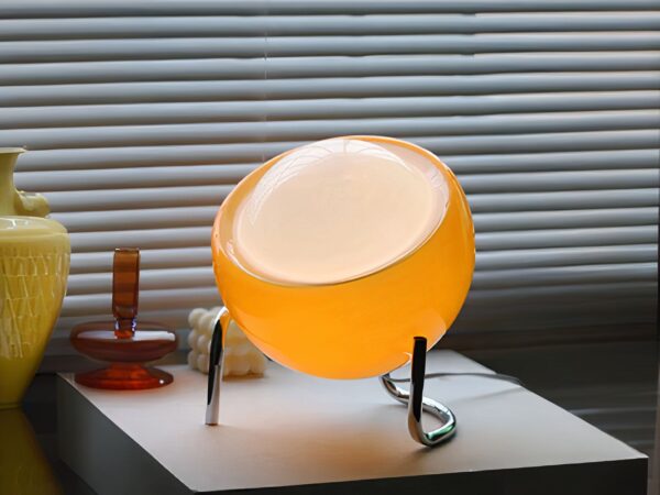 Lampe à poser LED orange tactile et sphérique, sur une table blanche.