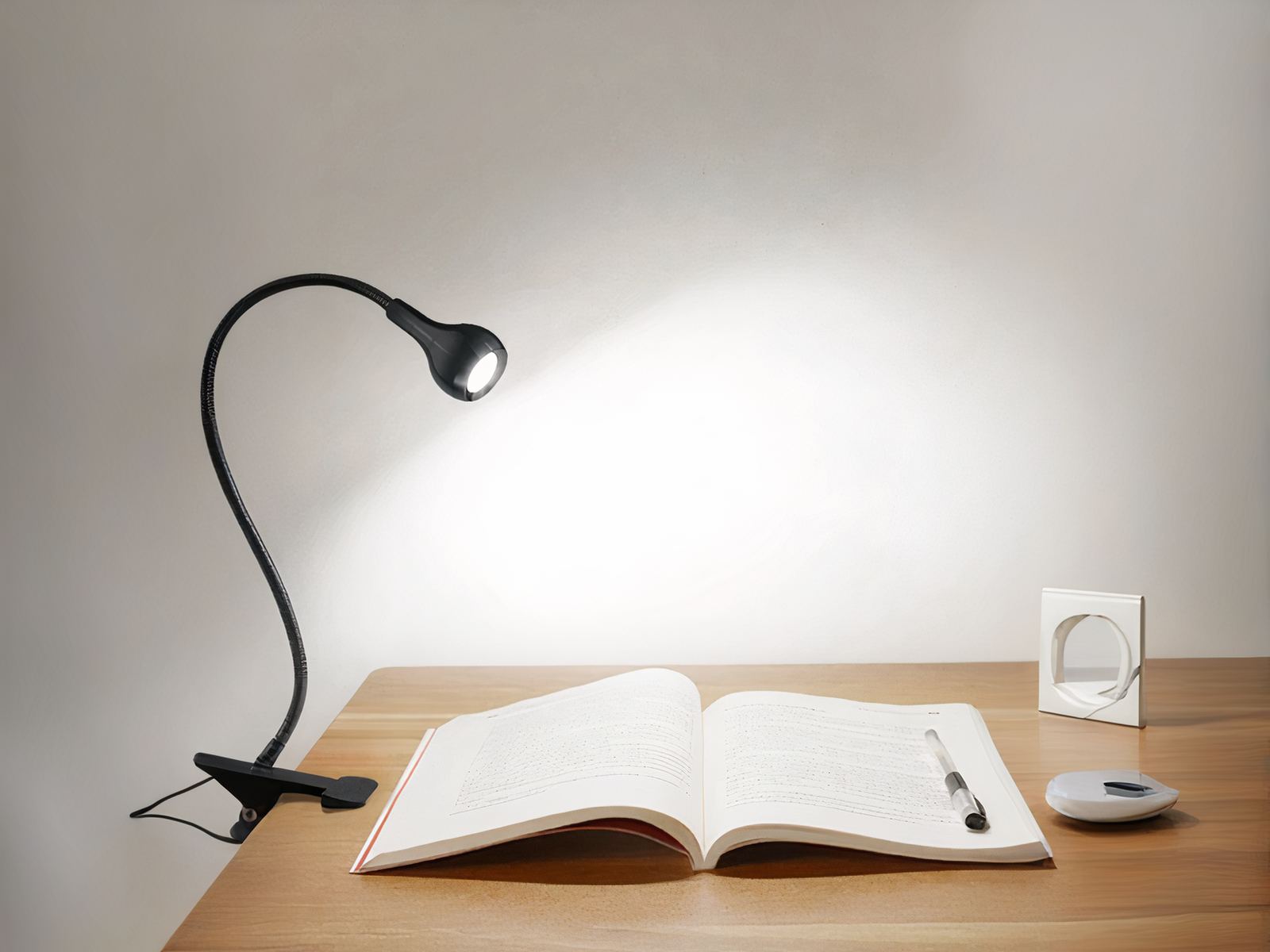Lampe de bureau LED noir flexible et réglable allumée à un bureau avec un livre posé sur le bureau