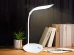Lampe de bureau LED tactile et design allumée sur un bureau dans le noir avec des livres posés à côté