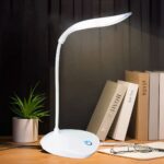 Lampe de bureau LED tactile et design Lampe de bureau LED tactile et design allumée sur un bureau dans le noir avec des livres posés à côté