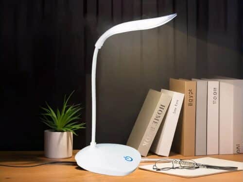 Lampe de bureau LED tactile et design allumée sur un bureau dans le noir avec des livres posés à côté