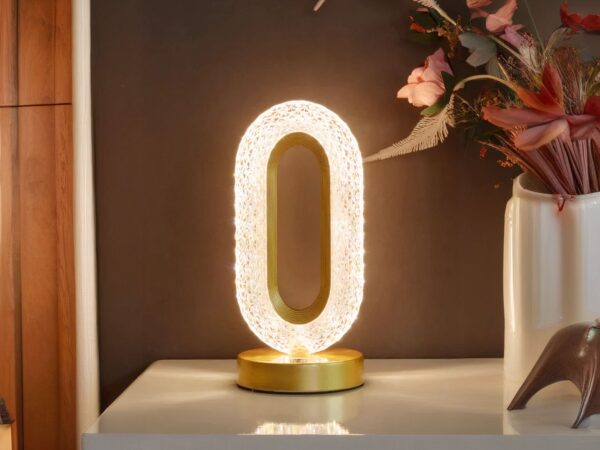 Lampe de chevet LED design en métal doré, sur une table.